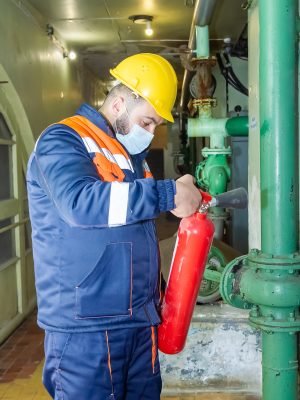 A caucasian mechanical engineer holding a fire extinguisher in uniform and protective helmet