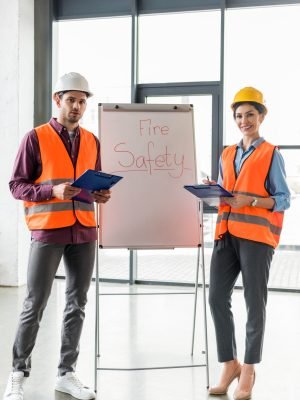 selective focus of fireman standing near attractive coworker near white board with fire safety