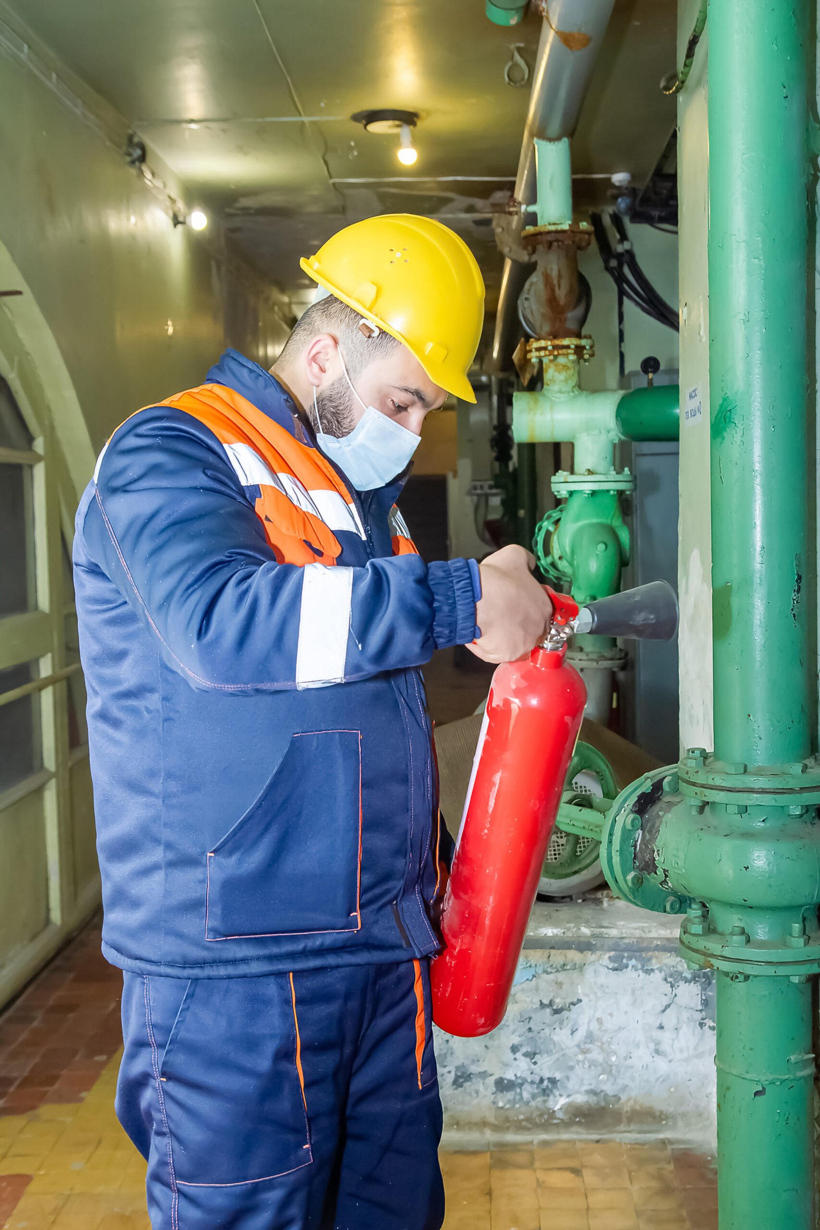 A caucasian mechanical engineer holding a fire extinguisher in uniform and protective helmet